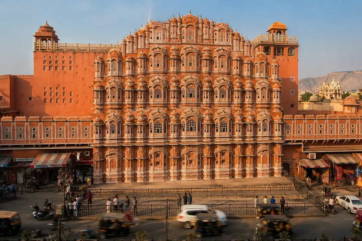 Front view of Hawa Mahal in Jaipur, Rajasthan, featuring its iconic pink sandstone façade with hundreds of ornate windows illuminated by warm afternoon sunlight.
