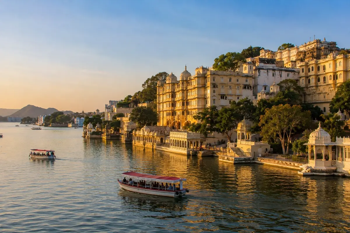 Golden-hour view of Lake Pichola in Udaipur featuring heritage palaces, lakeside ghats, traditional boat rides, and reflections shimmering across the tranquil waters.