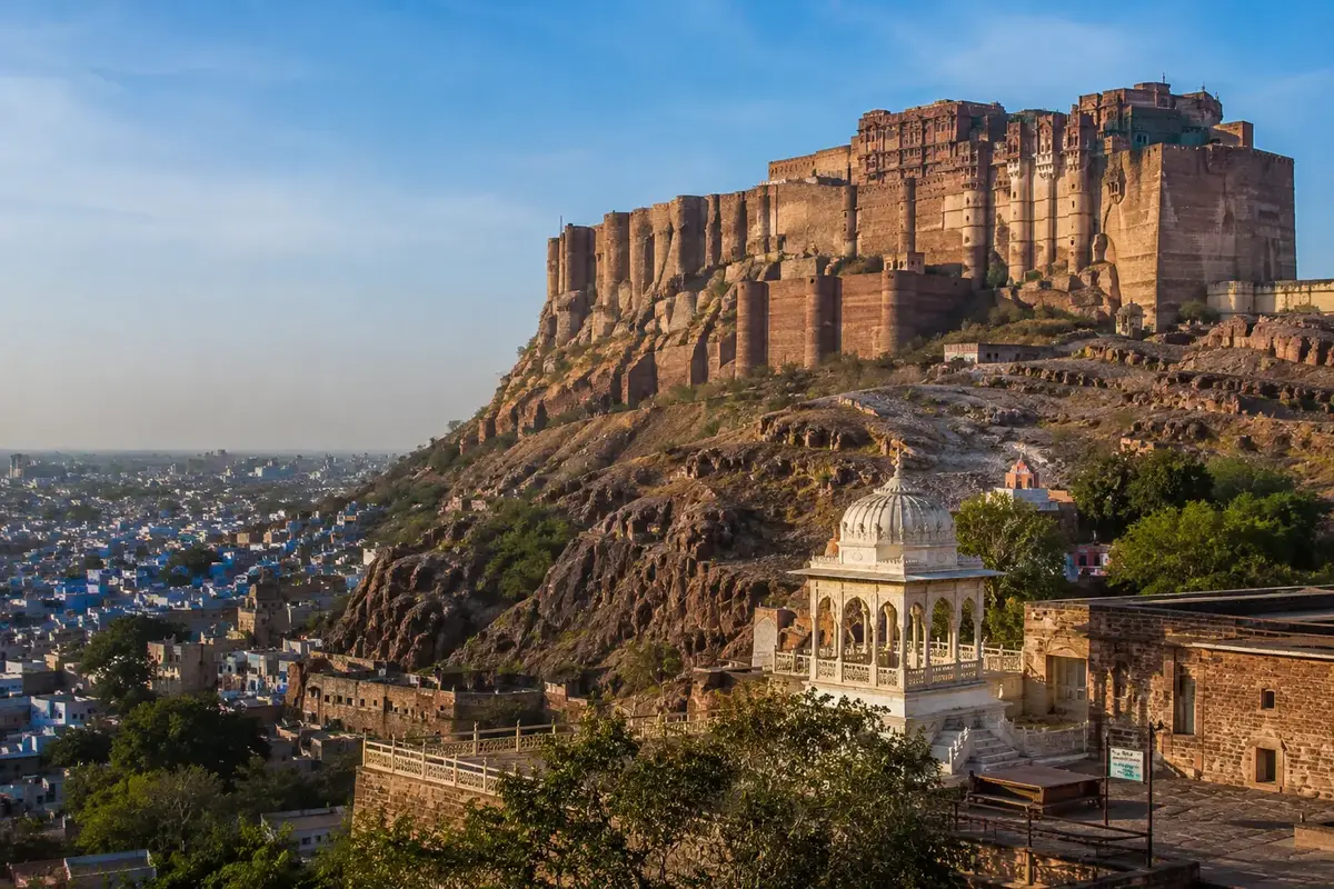 Panoramic view of Mehrangarh Fort towering above Jodhpur's blue houses, showcasing massive sandstone walls and historic Rajput architecture under warm daylight.