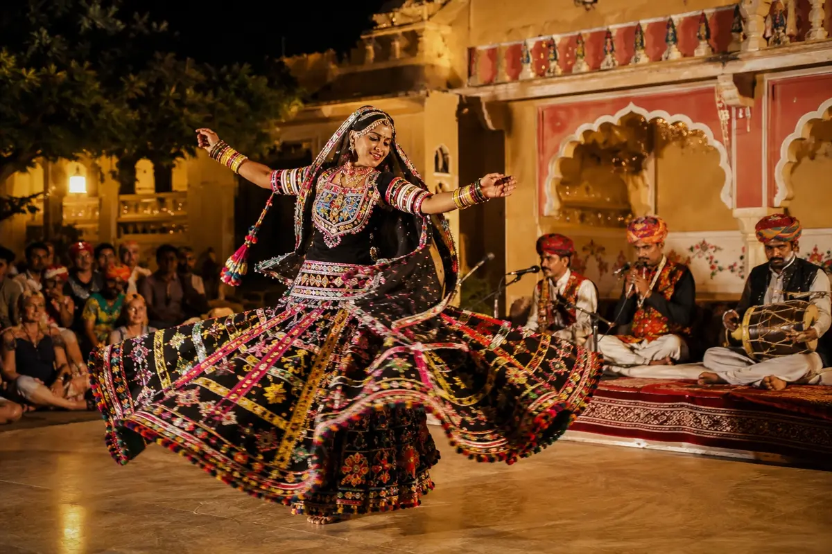 Traditional Rajasthani folk dancer performing a vibrant cultural dance show with live musicians and audience in a heritage setting.